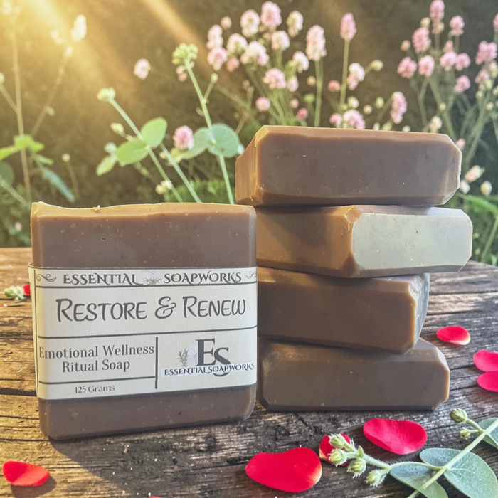 Restoration & Renewal Emotional Wellness Soap on a wooden surface with flowers in the background.