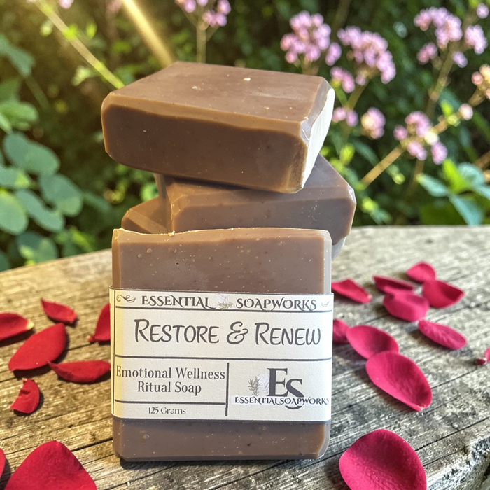 Restoration & Renewal Emotional Wellness Soap on a wooden surface with flowers in the background.