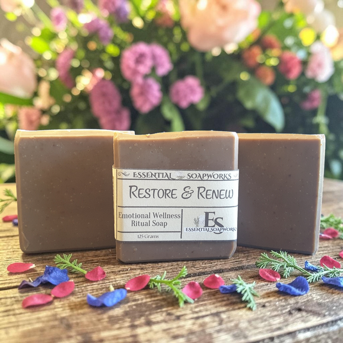 Restoration & Renewal Emotional Wellness Soap on a wooden surface with flowers in the background.