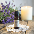 Restore & Renew Emotional Wellness Oil on a doily on a wooden surface with lavender and candles
