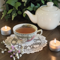 Detox tea in a tea cup with teapot, candles, and flowers on a wooden table