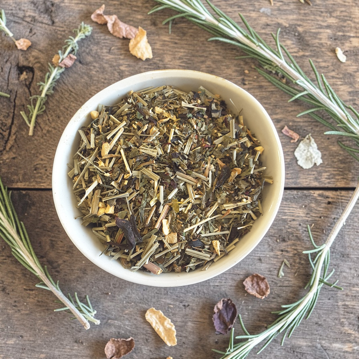 Detox loose leaf tea mix in a white bowl on a wooden surface with herbs around