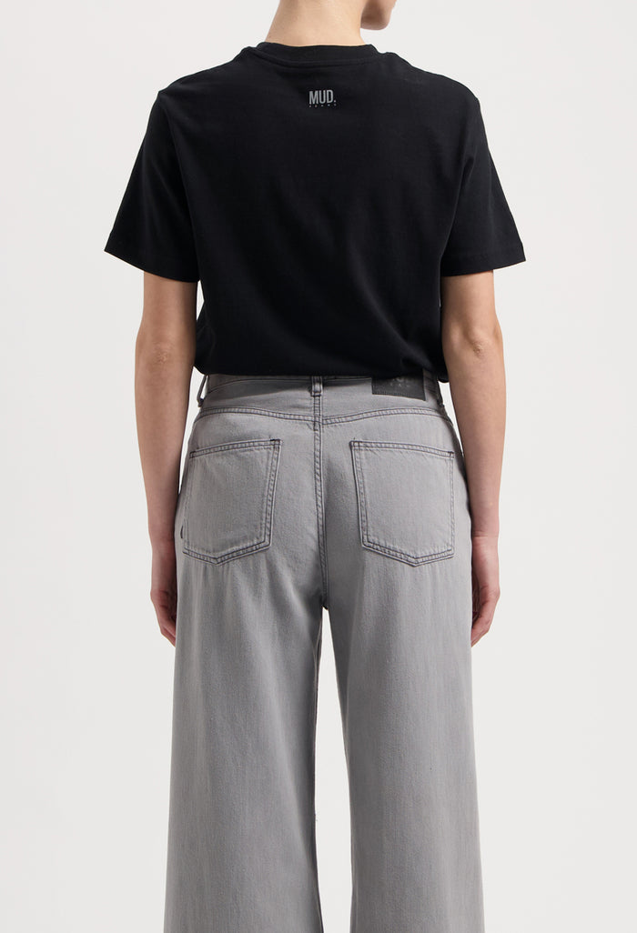 Sustainable MUD Jeans in dark brown, crafted from organic cotton, worn with a white t-shirt and white sneakers.