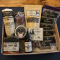 A Samhain ritual kit filled with various natural products including soap, ritual oil, tea, dried flowers, and herbal bundles, arranged in a cardboard tray on a dark surface.