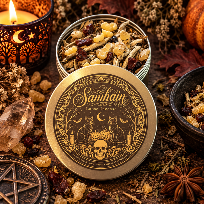 A round metal tin of Samhain Loose Incense is shown open with the lid in front, surrounded by autumn herbs, crystals, dried flowers, a candle, and spices on a rustic surface. The lid features a detailed gold illustration of cats, pumpkins, a skull, and a crescent moon on a black background, with the words 'Samhain Loose Incense' printed above.