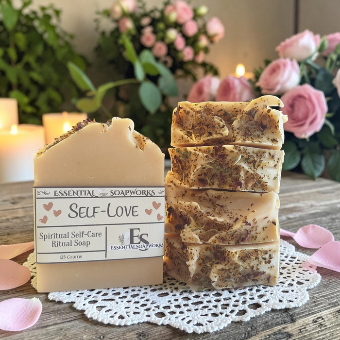 four bars of self love soap on a doily on a wooden surface with roses and candles in the background