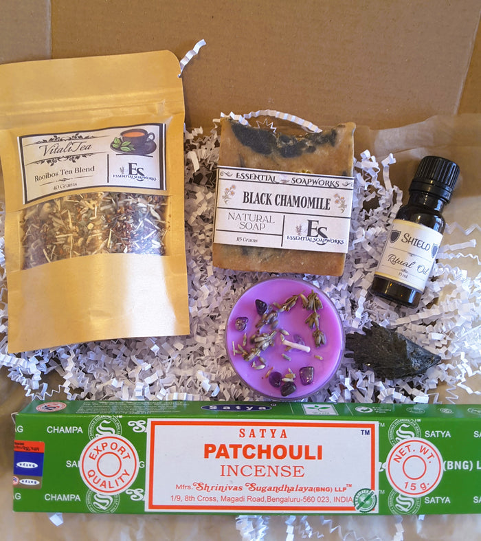 Spiritual Self-Care Mystery Kit including tea, soap, essential oil, and incense on a cardboard background.