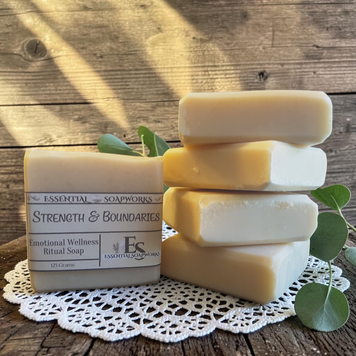 Strength & Boundaries Emotional Wellness Soap on a white doily, surrounded by green leaves on a wooden surface.