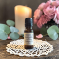 Strength & Boundaries Emotional Wellness Oil on a doily on a wooden surface with flowers and candles in the background