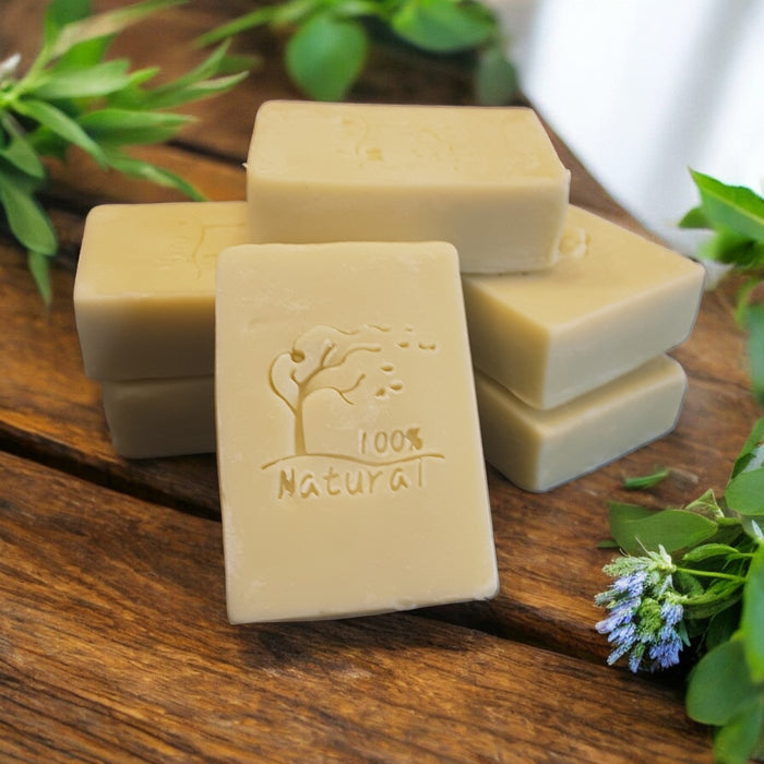 Four bars of natural soap with a tree stamp on a wooden surface surrounded by greenery.