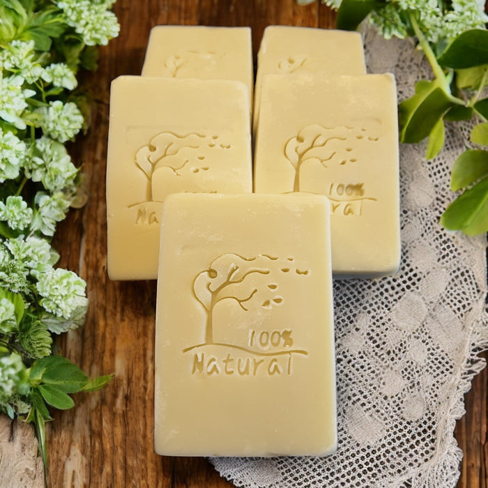 Three bars of 100% natural soap on a wooden surface with greenery