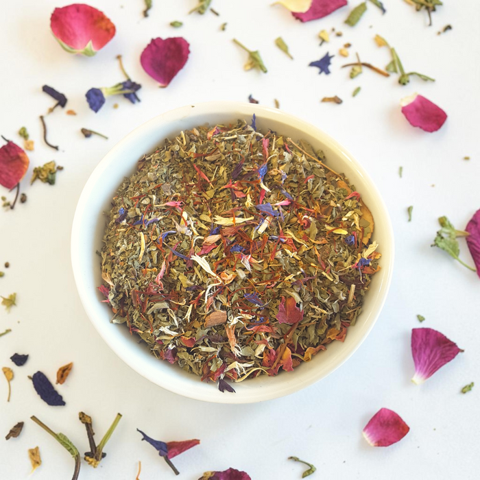 Loose leaf Temple Garden tea in a white bowl with scattered petals on a light background