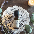 Tender Truth Emotional Wellness Oil on a doily on a wooden surface with lavender and eucalyptus