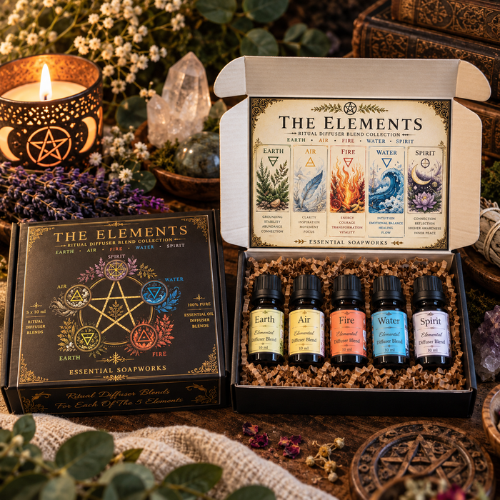 A boxed set of five element diffuser blends shown open with the five bottles in front of the branded box, styled on a rustic surface with a lit candle, crystals, dried flowers, and a decorative sign. The set is labeled 'The Elements' and includes Earth, Air, Fire, Water, and Spirit