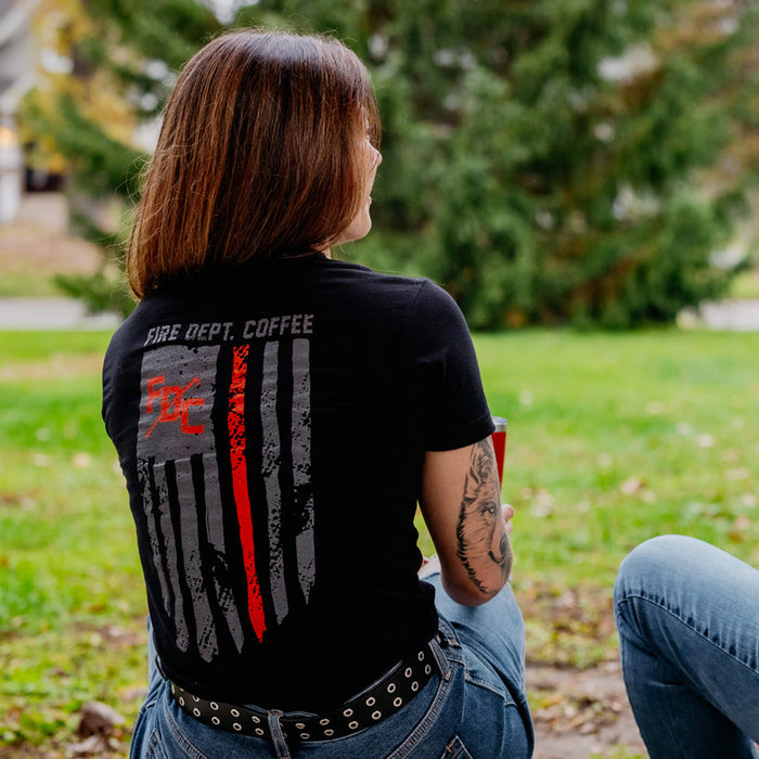 A lifestyle image of someone wearing the Thin Red Line Shirt. The back of the shirt features the thin red line flag with the FDC pike pole logo and text that reads "Fire Dept. Coffee"