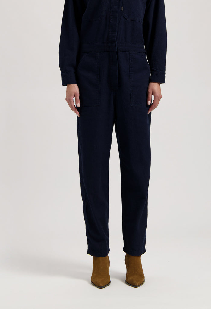 Dark navy long-sleeve jumpsuit with front pockets, paired with brown suede ankle boots.