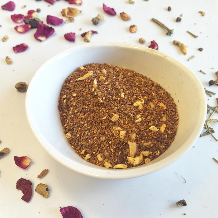 loose leaf uplifting tea blend in a white bowl surrounded by dried rose petals and herbs on a light background