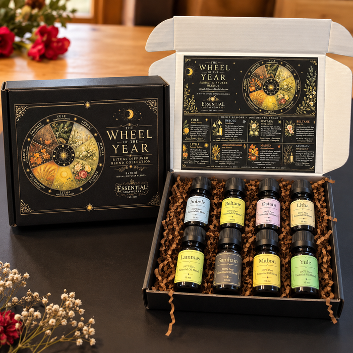 An open black gift box labeled 'The Wheel Year' with six small essential oil bottles arranged in brown paper shred, shown beside the matching closed box on a dark tabletop. The inside lid features a printed wheel diagram, and the bottles have colorful labels.