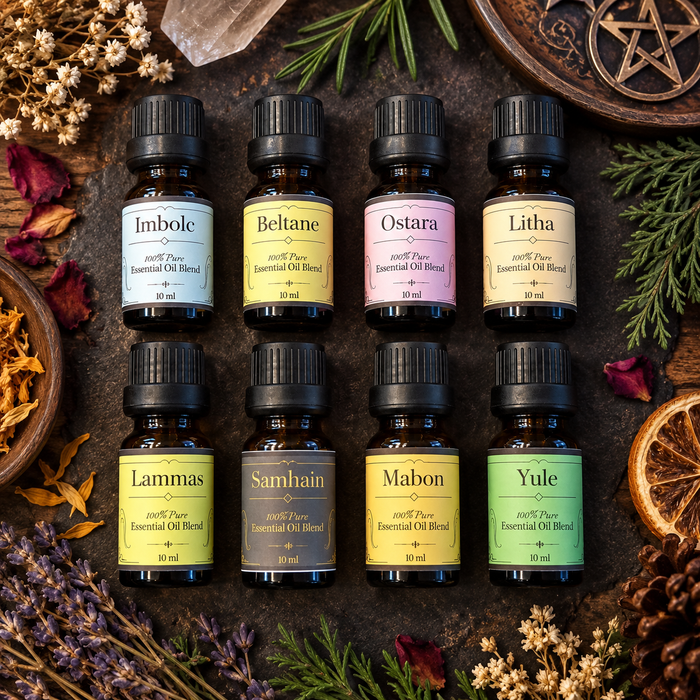 Eight small essential oil bottles arranged in two rows on a dark rustic surface, surrounded by dried flowers, greenery, and a wooden star motif. The bottles have black caps and labels in different pastel and earthy colors, including Imbolic, Beltane, Ostara, Litha, Lammas, Samhain, Mabon, and Yule.