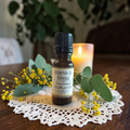 Worthy & Whole Emotional Wellness Oil on a doily on a wooden surface with yellow flowers and a candle in the background