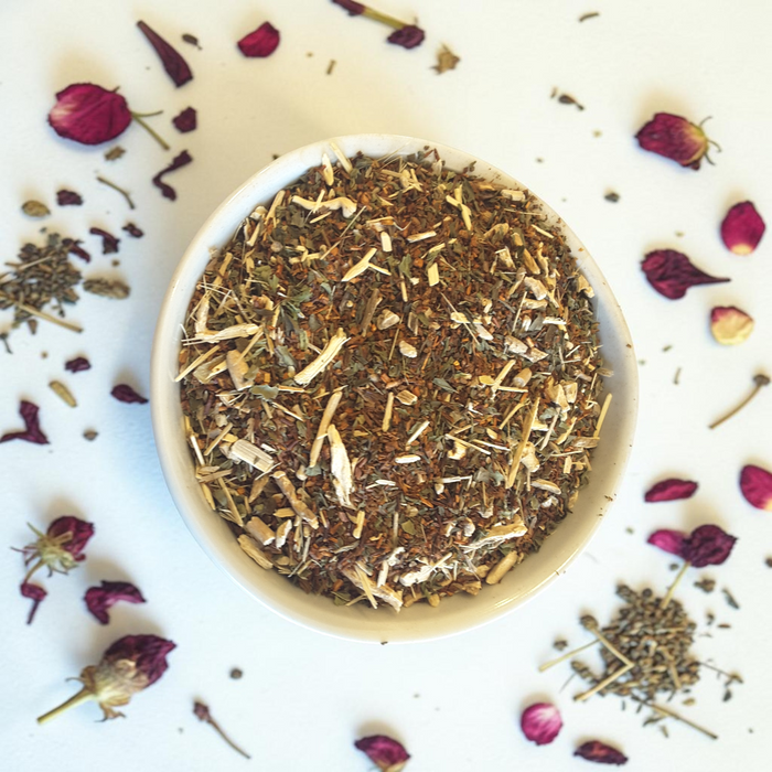 Loose leaf Divine Masculine tea blend in a bowl with dried herbs and flowers on a white background